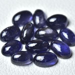 May include: A group of twelve oval-shaped, dark blue gemstones. The gemstones are smooth and polished, with a slight sparkle.