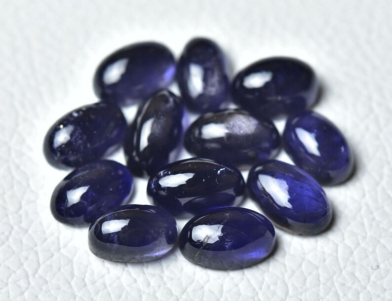 May include: A group of twelve oval-shaped, dark blue gemstones. The gemstones are smooth and polished, with a slight sparkle.