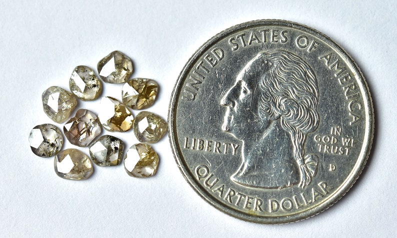 May include: A group of 12 small, rough-cut, light brown diamonds, with some black inclusions, next to a US quarter for size comparison.