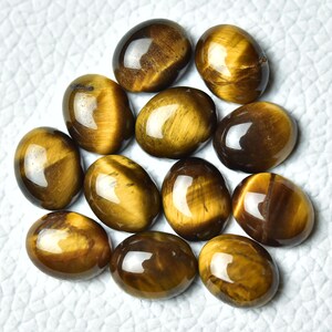 K&ouml;nnte beinhalten: Eine Sammlung von 12 ovalen Tigeraugen-Edelsteinen. Die Steine sind eine Mischung aus goldbraunen und braunen Farben mit einem chatoyanten Effekt.