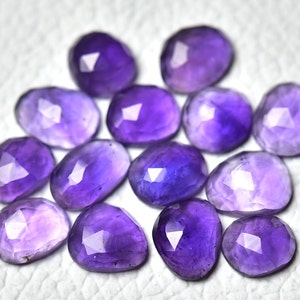 May include: A collection of 12 faceted amethyst gemstones in various shades of purple. The gemstones are oval shaped and have a smooth, polished finish.