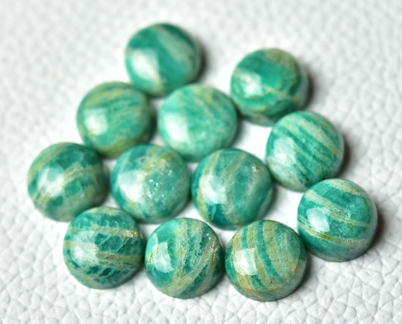 May include: A collection of 12 round, green and white amazonite cabochons. The cabochons are smooth and polished, with a variety of green and white patterns.