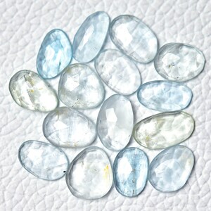 Puede incluir: Una colecci&oacute;n de 15 piedras preciosas de aguamarina azul claro, cada una con una forma ovalada facetada &uacute;nica. Las piedras est&aacute;n dispuestas sobre una superficie blanca.