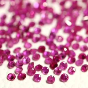 Könnte beinhalten: Eine Streuung kleiner, runder, rosafarbener Edelsteine auf einer weißen Oberfläche. Die Edelsteine sind in verschiedenen Rosatönen, von hell bis dunkel.