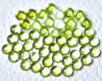 May include: A collection of round, green peridot gemstones, each with a smooth, polished surface. The stones are arranged in a circular pattern on a white background.