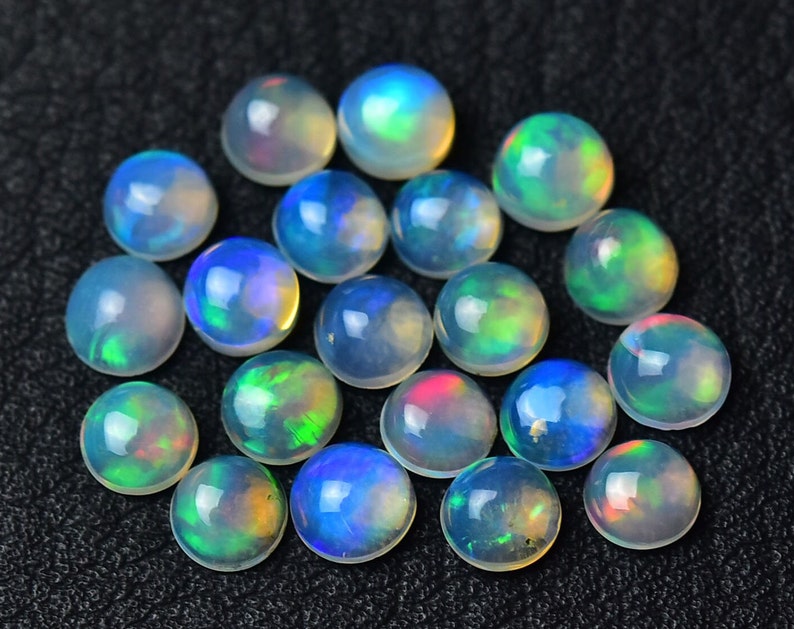 May include: A collection of round, iridescent opal cabochons in various shades of blue, green, and white. The opals are smooth and polished, with a high gloss finish.