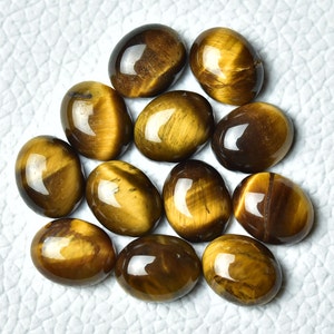 K&ouml;nnte beinhalten: Eine Sammlung von 12 ovalen Tigeraugen-Edelsteinen. Die Steine sind eine Mischung aus braunen und goldenen Farben mit einem chatoyanten Effekt.