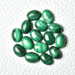 May include: A collection of 15 oval-shaped malachite gemstones. The stones are a deep green color with intricate patterns of lighter and darker green.