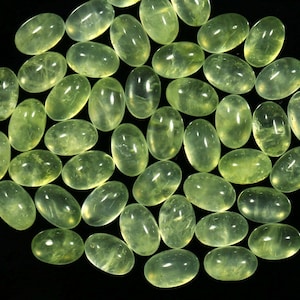 May include: A collection of 30 oval-shaped green gemstones, also known as green aventurine, arranged in a circular pattern on a black background.