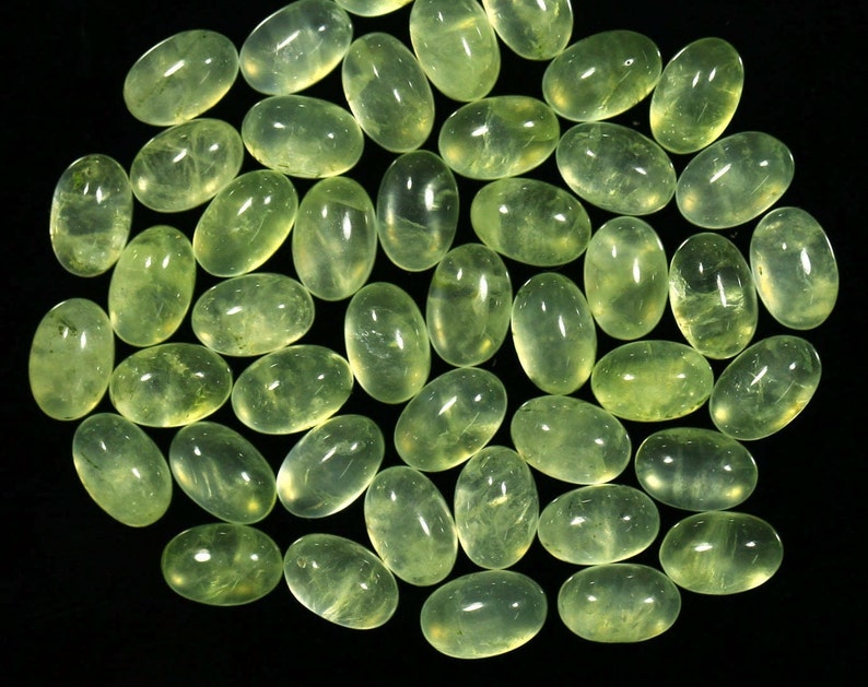 May include: A collection of 30 oval-shaped green gemstones, also known as green aventurine, arranged in a circular pattern on a black background.