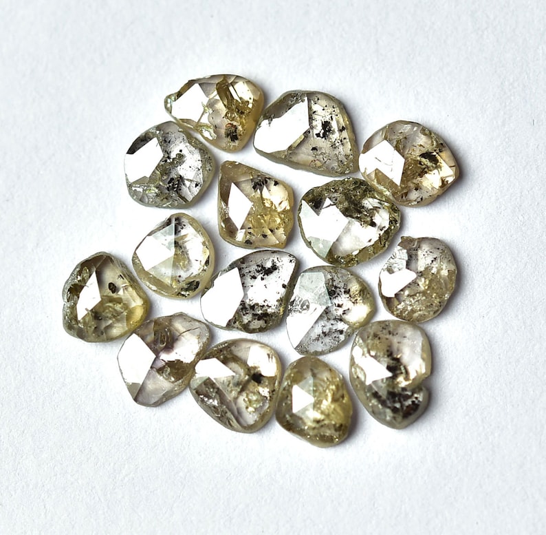 May include: A collection of 14 rough, faceted, and translucent diamonds with a light green and gray color.