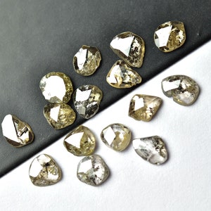 May include: A collection of 15 rough, unpolished, natural diamonds. The diamonds are various shades of grey and brown, and have a faceted, irregular shape.