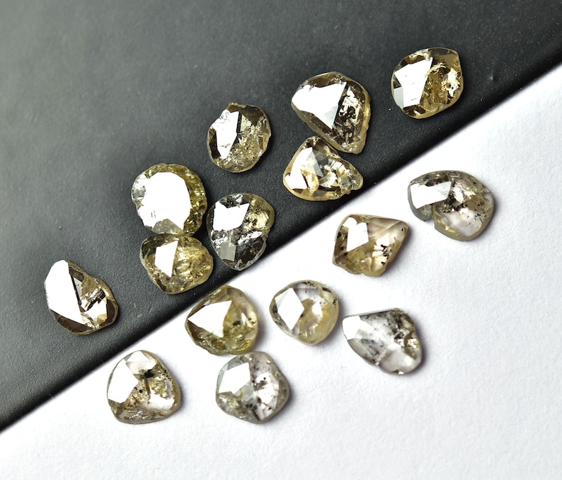 May include: A collection of 15 rough, unpolished, natural diamonds. The diamonds are various shades of grey and brown, and have a faceted, irregular shape.