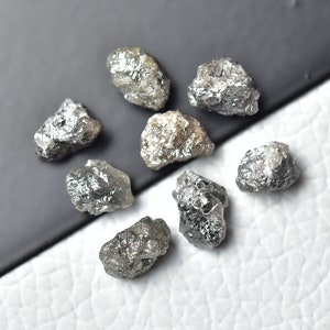 May include: A collection of seven rough, uncut, grey diamonds. The diamonds are various sizes and shapes, and have a silvery sheen.