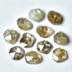 May include: Ten rough cut, brown diamonds with a variety of shapes and sizes. The diamonds are arranged in a circle on a white background.