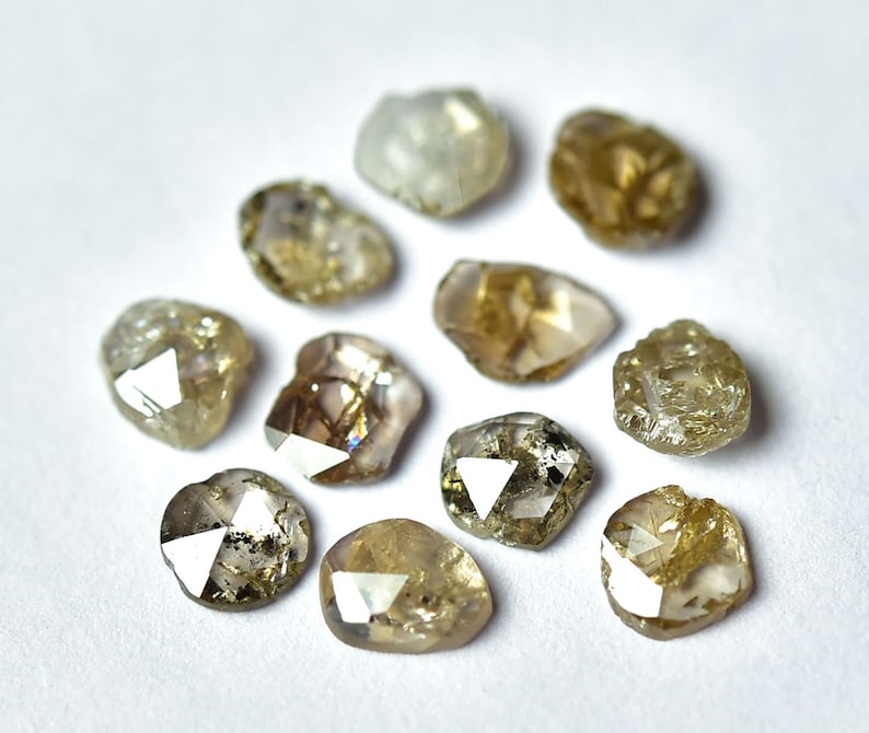 May include: Ten rough cut, brown diamonds with a variety of shapes and sizes. The diamonds are arranged in a circle on a white background.