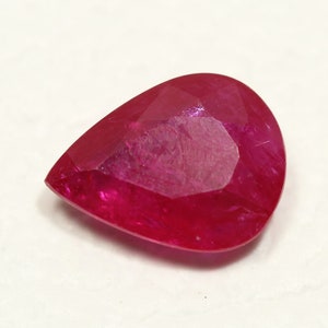 May include: A vibrant red pear-shaped gemstone with a faceted cut.