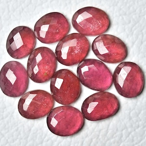 Peut inclure: Plusieurs pierres précieuses ovales et facettées, de nuances rouges et roses. Les gemmes sont disposées sur une surface blanche, mettant en valeur leurs facettes polies et leur clarté interne. Idéal pour la création de bijoux.