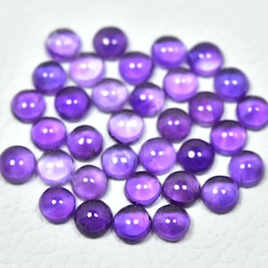 May include: A collection of 25 round, purple amethyst cabochons. The cabochons are smooth and polished, with a slight variation in color and size.
