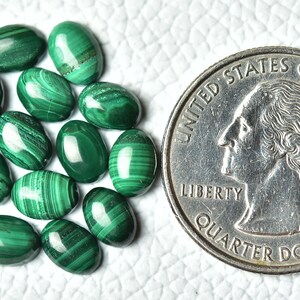 May include: A collection of 14 oval-shaped malachite gemstones, each with a unique green and white pattern. The stones are arranged in a cluster and are approximately the size of a US quarter.