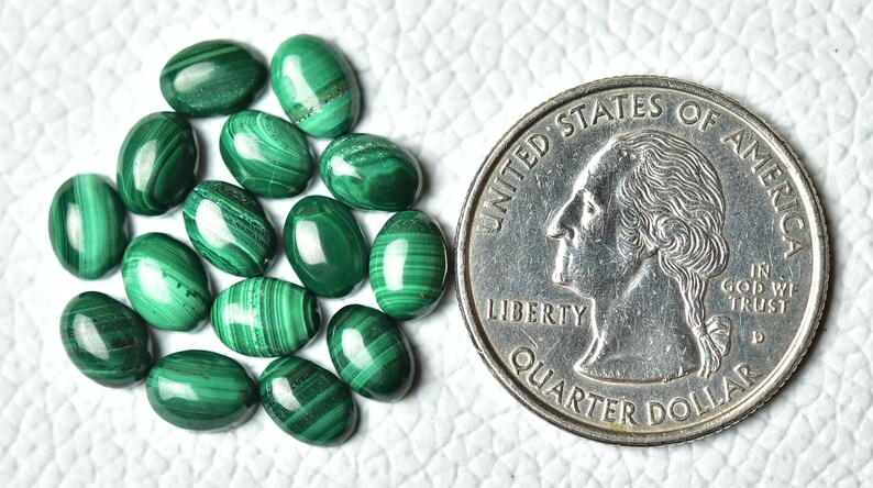 May include: A collection of 14 oval-shaped malachite gemstones, each with a unique green and white pattern. The stones are arranged in a cluster and are approximately the size of a US quarter.
