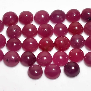 Op de afbeelding: Een verzameling van 30 ronde, cabochon geslepen, roze robijn edelstenen. De stenen zijn allemaal ongeveer even groot en hebben een gladde, gepolijste afwerking.