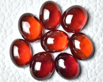 May include: Eight oval-shaped, polished gemstones with a deep red-orange hue. The gems are arranged in a circular pattern, each displaying a glossy, translucent appearance. The stones are likely garnets, suitable for jewelry making.
