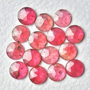 以下が含まれることがあります： 白い表面にランダムに配置された、ファセットカットの丸い形をしたピンクの宝石カボション14個のセットです。