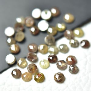 Op de afbeelding: Een verzameling bruine, grijze en gele ruwe diamanten, ook wel ruwe diamanten genoemd, met een gefacetteerde, ronde vorm. Deze diamanten zijn perfect voor het maken van sieraden en handwerk.