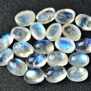 May include: A collection of oval-shaped moonstone cabochons, with a milky white color and iridescent blue flashes.