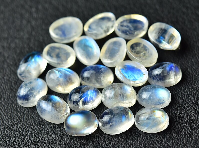 May include: A collection of oval-shaped moonstone cabochons, with a milky white color and iridescent blue flashes.