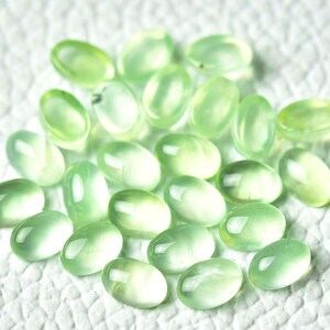 May include: A collection of oval-shaped, light green gemstones. The stones are smooth and polished, with a translucent appearance.