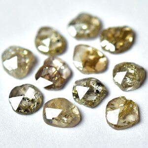 May include: A collection of ten faceted, rough-cut, light brown diamonds. The diamonds are arranged in a circle on a white surface.