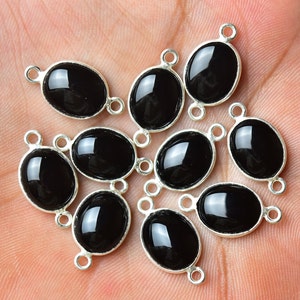 May include: Ten black oval gemstone beads with silver-toned connector loops. The beads are smooth and shiny.
