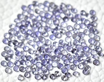 May include: A large quantity of small, round, purple gemstones. The gemstones are scattered on a white surface.