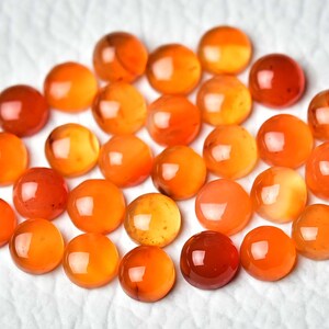 Pu&ograve; includere: Una collezione di pietre preziose rotonde e lucide in tonalit&agrave; arancioni e rosse. Le pietre sono disposte su una superficie bianca, mettendo in risalto le loro superfici lucide e riflettenti. Le pietre variano in intensit&agrave; di colore.