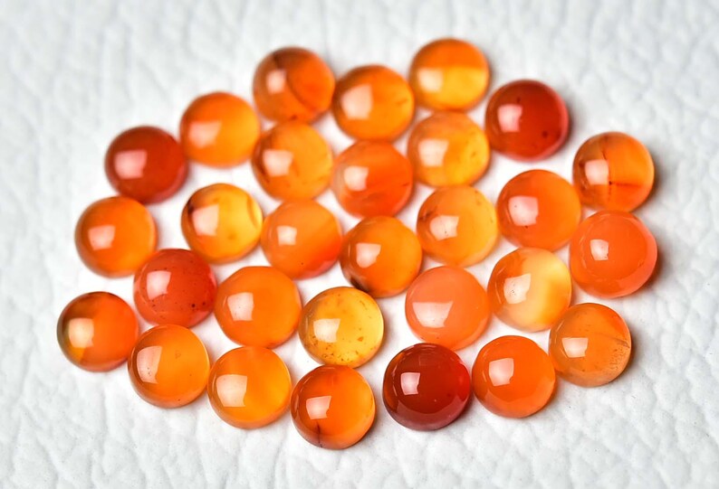 Pu&ograve; includere: Una collezione di pietre preziose rotonde e lucide in tonalit&agrave; arancioni e rosse. Le pietre sono disposte su una superficie bianca, mettendo in risalto le loro superfici lucide e riflettenti. Le pietre variano in intensit&agrave; di colore.
