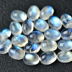 May include: A collection of oval-shaped moonstone cabochons, with a milky white color and iridescent blue flashes.