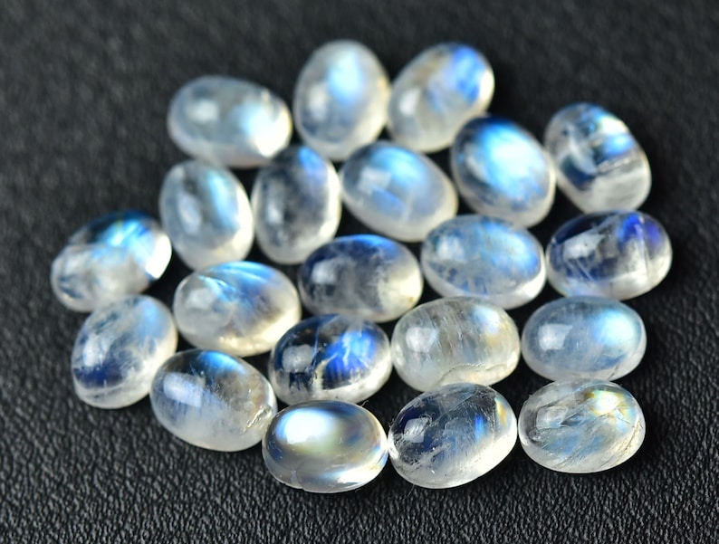 May include: A collection of oval-shaped moonstone cabochons, with a milky white color and iridescent blue flashes.