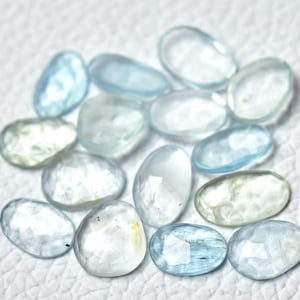 Puede incluir: Una colecci&oacute;n de piedras preciosas de aguamarina azul claro, cada una con una forma facetada &uacute;nica. Las piedras son lisas y pulidas, con una apariencia transl&uacute;cida.