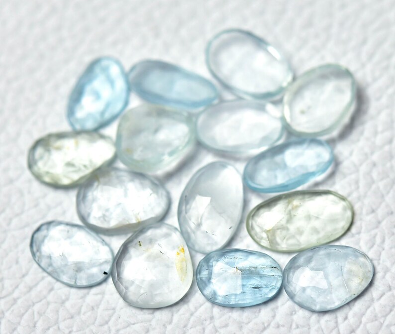 Puede incluir: Una colecci&oacute;n de piedras preciosas de aguamarina azul claro, cada una con una forma facetada &uacute;nica. Las piedras son lisas y pulidas, con una apariencia transl&uacute;cida.