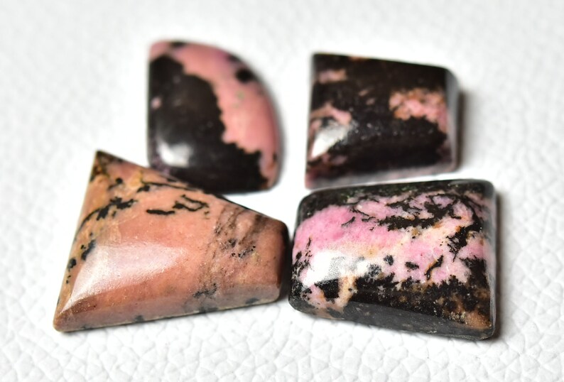 May include: Four pink and black gemstone cabochons in different shapes, including a triangle, a square, and two half-circles.