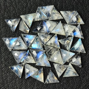 May include: A collection of iridescent rainbow moonstone triangular gemstone cabochons. The stones are faceted and have a translucent, milky white color with flashes of blue, green, and gold.