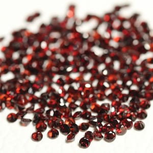 Può includere: Un mucchio di piccole pietre preziose rosso scuro. Le pietre preziose sono rotonde e hanno una finitura lucida e lucidata.