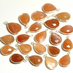 Könnte beinhalten: Eine Sammlung von 20 orangefarbenen Edelstein-Tropfenanhängern mit silberfarbenen Zargen und Sprungringen. Die Anhänger sind auf einer weißen Oberfläche verstreut.
