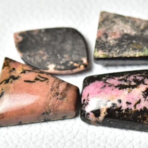 May include: Four cabochon cut gemstones with pink and black patterns. The stones are cut in different shapes, including a triangle, a rectangle, and two ovals.