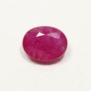 May include: A vibrant pink oval-shaped gemstone with a faceted cut. The gemstone has a slightly cloudy appearance.