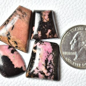 May include: Four pink and black cabochon gemstones, with a US quarter for size comparison.