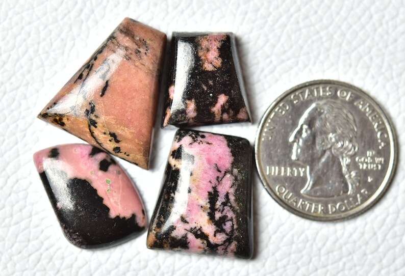 May include: Four pink and black cabochon gemstones, with a US quarter for size comparison.