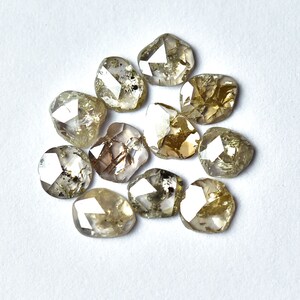May include: A collection of twelve rough, faceted, natural diamonds. The diamonds are a light brown color with a translucent appearance. The diamonds are arranged in a circular pattern on a white surface.